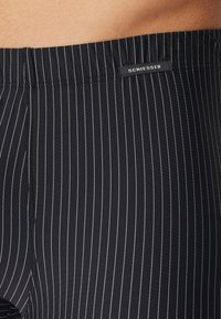 Costumini da bagno neri con strisce verticali bianche, dotati di una cintura elastica e di una piccola etichetta "SCHIESSER" sul lato.