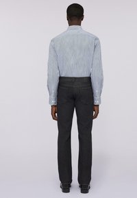 Camisa de botones a rayas en tonos de azul, combinada con pantalones de mezclilla oscuros. El diseño presenta un corte clásico y una silueta estructurada.