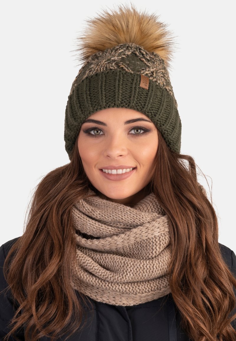 Beanie a maglia verde oliva con pom-pom in pelliccia artificiale crema e design intrecciato, abbinato a una sciarpa infinita beige a maglia.