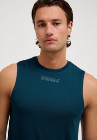 Mouwloos sportshirt in donker te groen, gemaakt van gladde stof. Kenmerkt zich door een ronde hals en het "HUMMEL" logo dat op de borst is gedrukt.