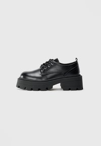 Black leather shoes with a rounded toe, lace-up design, and a chunky rubber sole featuring deep treads. Simple stitching detail along edges.
