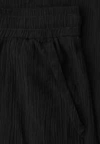 Tissu noir texturé avec une ceinture élastique et une poche latérale avec des coutures visibles sur un pantalon ou un short.