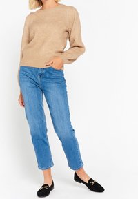 Beige stickad tröja med diamantsmönster, rund halsringning och ribbade muddars, parat med ljusblå raka jeans och svarta loafers.