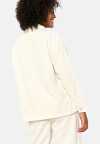 Cream corduroy jacket with a relaxed fit, button cuffs, and a classic collar, featuring horizontal ribbed texture and side seam details.