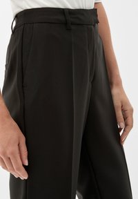Schwarze maßgeschneiderte Hose mit hoher Taille, seitlichen Taschen, Falten und einer glatten Textur. Verfügt über Gürtelschlaufen und einen Bügelfalte an der Vorderseite.
