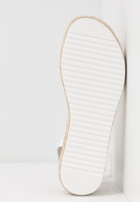 Chaussure espadrille blanche avec une semelle en caoutchouc texturée et striée et un bord en jute tressé, présentée sur le côté sur un fond uni.