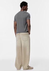 Siva kratka majica s kratkimi rokavi v kombinaciji z ohlapnimi bež kavbojkami iz džinsa, ki imajo velike žepne in sproščen kroj, pogled od zadaj.