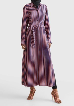 Robe longue rayée en bleu marine et rose, avec un devant à boutons, une taille à nouer et des manches longues. Portée avec des talons roses à lanières.