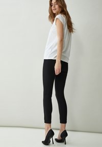 Top bianco a maniche corte abbinato a pantaloni neri alla caviglia e scarpe con tacco alto nere. Tessuti morbidi, design aderente, dettagli minimi.