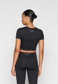 Black activewear top with short sleeves, cropped design, smooth texture, and branding on the back. Paired with high-waisted black leggings.