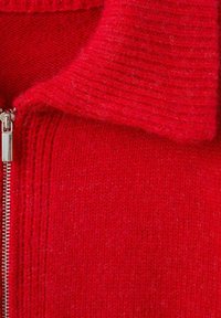 Maglione rosso lavorato a maglia con chiusura a zip frontale, caratterizzato da un colletto a coste e una texture del corpo, che mette in evidenza il materiale morbido e peluche.
