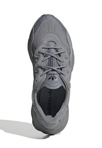 Scarpa atletica grigia con tomaia in mesh e suede, punte rotonde e suola texturizzata. Presenta lacci e etichetta con logo sulla linguetta.