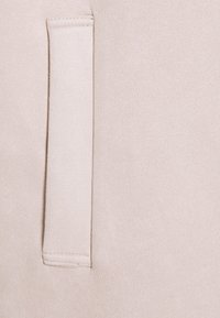 Jasnobeżowa tkanina o miękkiej, teksturowanej powierzchni. Zawiera małą, prostokątną kieszeń z czystym przeszyciem wzdłuż krawędzi.