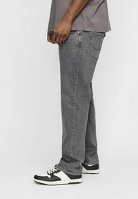 Gray denim jeans with a straight fit, featuring back pockets and stitched detailing, paired with black and white sneakers.