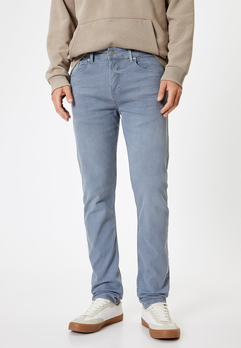 Jeans de denim de color azul claro con un ajuste slim, que cuentan con cinco bolsillos y un cierre delantero con botón. Combinados con una sudadera beige y zapatillas blancas.