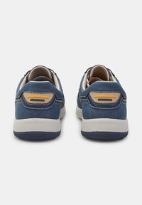 Adidași din suede albastru cu accente crem, talpă din cauciuc texturată și detaliu galben pe toc. Formă rotundă și design de tip low-top.