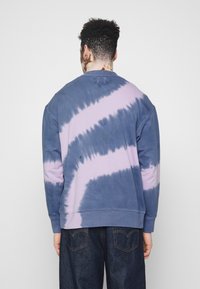 Felpa tie-dye in tonalità blu e lavanda, con scollatura rotonda, maniche lunghe e vestibilità comoda. Materiale in misto cotone con finitura testurizzata.