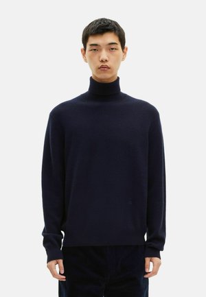 Granatowy sweter z golfem wykonany z miękkiego materiału. Posiada długie rękawy, luźny krój oraz ściągacze przy szyi, mankietach i dolnym brzegu. Brak widocznych logo.