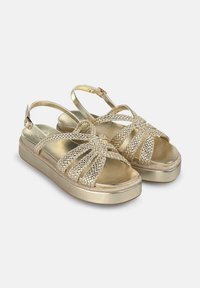 Gold sandals with a thick platform, featuring woven upper straps, adjustable slingback, and sparkling embellishments.