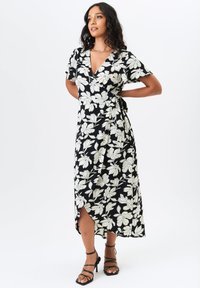 Black wrap dress featuring a white floral pattern, short sleeves, a V-neckline, and a side tie, with a slit on one side and soft fabric texture.