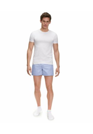 White short-sleeve fitted t-shirt paired with light blue striped shorts, worn with white socks; model stands upright, facing forward.