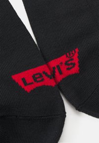 Svarta strumpor i texturerat material med en framträdande röd Levi's-logotyp över toppen. Enhetlig färg med släta sömmar.