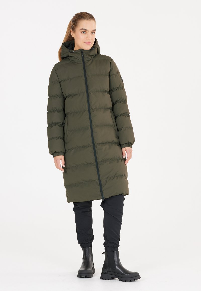 Abrigo acolchado en verde oliva oscuro, con cierre de cremallera frontal, capucha, puños elásticos y dos bolsillos laterales. Combinado con pantalones jogger negros y botas.