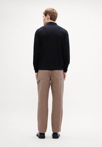 Μαύρο πλεκτό πόλο με γιακά, συνδυασμένο με ανοιχτό καφέ παντελόνι πλατύ. Λείο υφασμάτινο, casual σχέδιο και διακριτές λεπτομέρειες στις τσέπες.