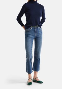 Laivastonsininen pooloneule, istuva; vaaleansiniset farkut, joissa repsottava helma; vihreä vyö; kiiltävät vihreät balleriinat. Korostuu yksinkertainen, klassinen muotoilu.