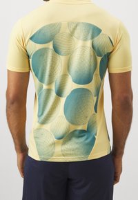 Pánská žlutá polo tričko s krátkým rukávem, na zadní straně s grafickým designem texturovaných tyrkysových kuliček, vyrobené z lehkého materiálu.