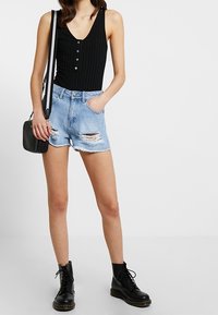 Black ribbed bodysuit with buttons, distressed light blue denim shorts, and black lace-up ankle boots. Small black crossbody bag.