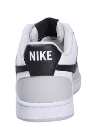 Nike sneaker featuring a white leather upper, black accents, padded collar, and textured gray heel panel with "NIKE" branding.