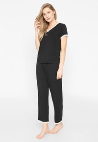 Ensemble de pyjama noir avec des manches courtes et des bordures en dentelle au col et aux poignets ; pantalon droit ; tissu en maille doux ; coupe décontractée.