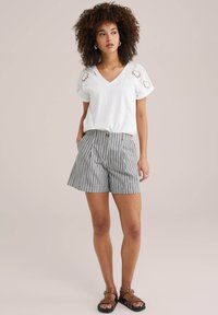 Witte korte mouwen V-hals top met oogjesdetails, gecombineerd met zwart-witte gestreepte shorts, ontworpen met zijzakken en een knoop aan de voorkant.