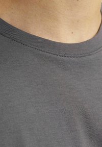 Camiseta de algodón gris con cuello redondo. La tela es suave con una apariencia ligeramente texturada y costuras uniformes a lo largo del cuello.
