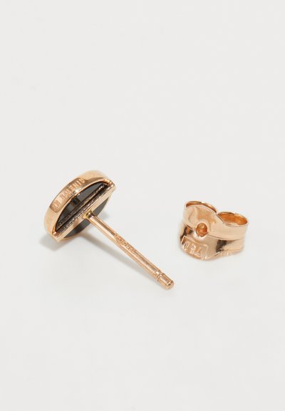 Korallenrosa dangle-Ohrringe mit einem runden, schwarzen Stecker und einem sichtbaren Stift sowie einem ringsförmigen Schädel mit eingravierten Details.
