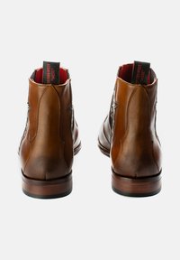 Braune Leder-Stiefeletten mit glatter Oberfläche, runder Zehenform und dunklem braunem Gummisohle. Rote Innenausstattung und Zuglaschen hinten.