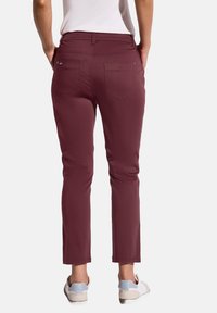 Burgundyfärgade byxor med slim fit, fem fickor och diskreta sömdetaljer, kombinerade med ljusa sneakers.