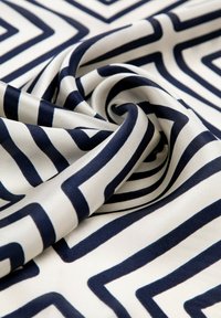 Tessuto con motivo che presenta uno sfondo crema e righe zigzag blu navy, superficie liscia e caduta fluida, mettendo in risalto il design geometrico.