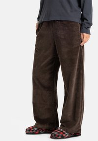 Bruine corduroy wijde broek met verticale ribbelstructuur. Gecombineerd met rode en zwarte geruite instapslippers.