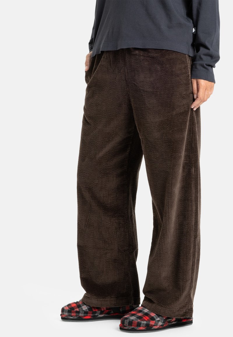 Bruine corduroy wijde broek met verticale ribbelstructuur. Gecombineerd met rode en zwarte geruite instapslippers.
