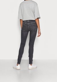 Jeans ajustados en denim gris oscuro, con una cintura alta, bolsillos traseros y un ajuste ceñido, combinados con una camiseta oversized gris claro y zapatos blancos.