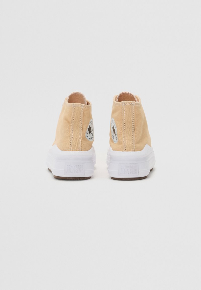 Zapatillas altas de lona beige con suelas de goma blanca, que presentan un logotipo circular en blanco y negro en los costados exteriores. Tejido texturizado.