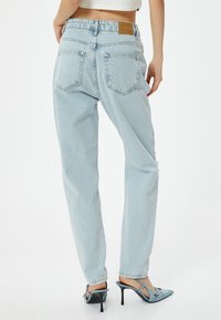 Högmidjade ljusblå denimjeans med en avslappnad passform, med bakfickor och en beige läderlapp vid midjan.