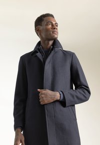 Abrigo de lana azul marino con cuello alto, cierre frontal de botones y bolsillos laterales. Presenta una silueta estructurada y puños acanalados.