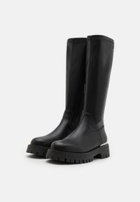 Botas de cuero negro hasta la rodilla con suela de goma gruesa, detalle de cremallera vertical y acabado suave. Diseño sencillo con costuras reforzadas.