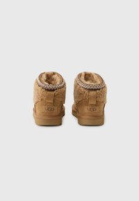 Bottes de chevilles en peau de mouton beige avec doublure douce, en forme arrondie et couture décorative autour du col. Logo UGG au niveau du talon.