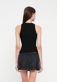 Svart ermeløs topp med en tettsittende design, sammen med et høyhøllet mørkt denim-skjørt med sidelommer og en lett utsvingt kant.