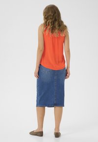 Haut sans manches rouge associé à une jupe midi en denim bleu. Le haut a une texture douce ; la jupe présente une coupe droite et des poches arrière.