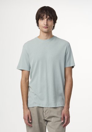 T-shirt azzurro chiaro a maniche corte con scollatura rotonda. Il tessuto sembra morbido con una vestibilità rilassata. Indossato con pantaloni chiari.